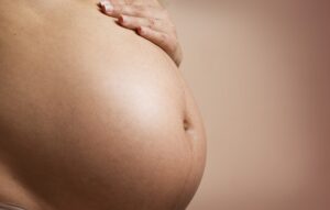 Barriga de mulher branca e grávida enquadrada no lado esquerdo da imagem.